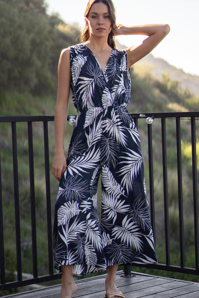 Tropical leaf printed jumpsuit. Has front pockets and adjustable back tie that is sleeveless. Elastic waistband and wide-leg design. Navy colored.