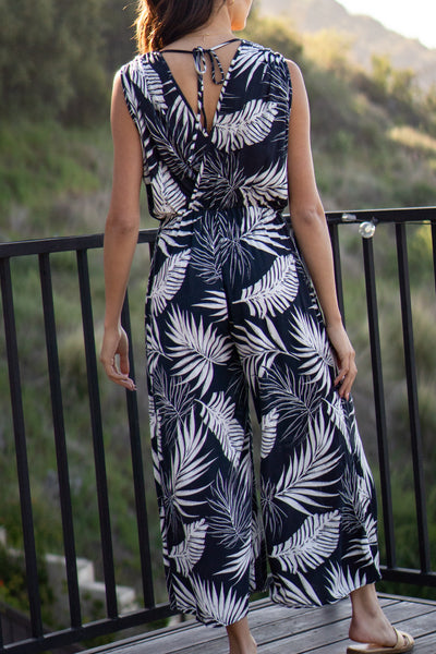 Tropical leaf printed jumpsuit. Has front pockets and adjustable back tie that is sleeveless. Elastic waistband and wide-leg design. Navy colored.