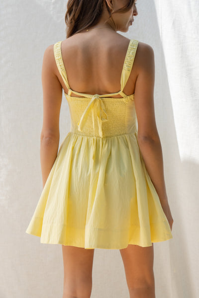 emilia flared mini dress has square neckline and flared silhouette. smocking on the back and adjustable back tie. comes in lemon and white.