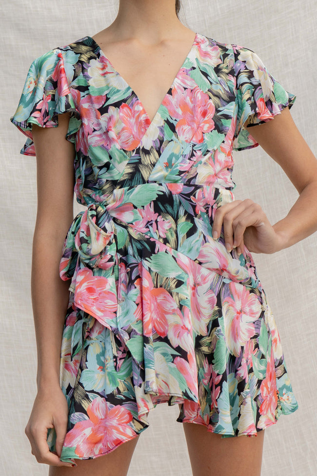 This Light Floral Wrap Dress features a flattering mini dress silhouette with wrap detail, tropical floral print, and an overlap V neckline. Short sleeves and light fabric make it perfect for warm-weather occasions.  