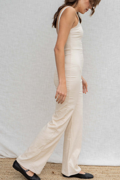 This fitted linen jumpsuit features tank sleeves and flare bottoms. beige color.