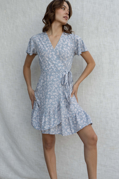 This mini dress features a playful wrap detail, short sleeves, and a flirty cross over neckline. With a fun floral print and ruffle detail.
